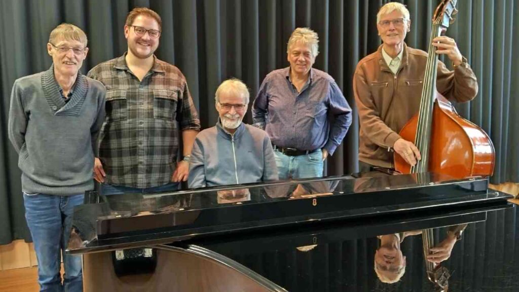 Fünf Männer posieren mit Klavier und Kontrabass in einem Musikraum. Eine musikalische Gruppe.