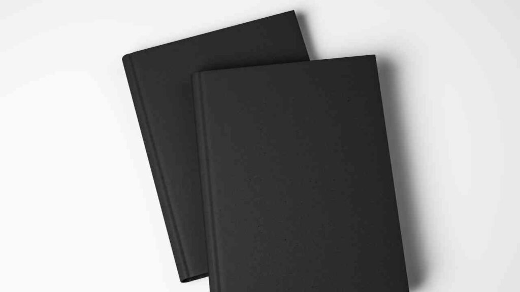 Zwei schwarze, unbeschriftete Bücher liegen überkreuzt auf einem weißen Hintergrund.