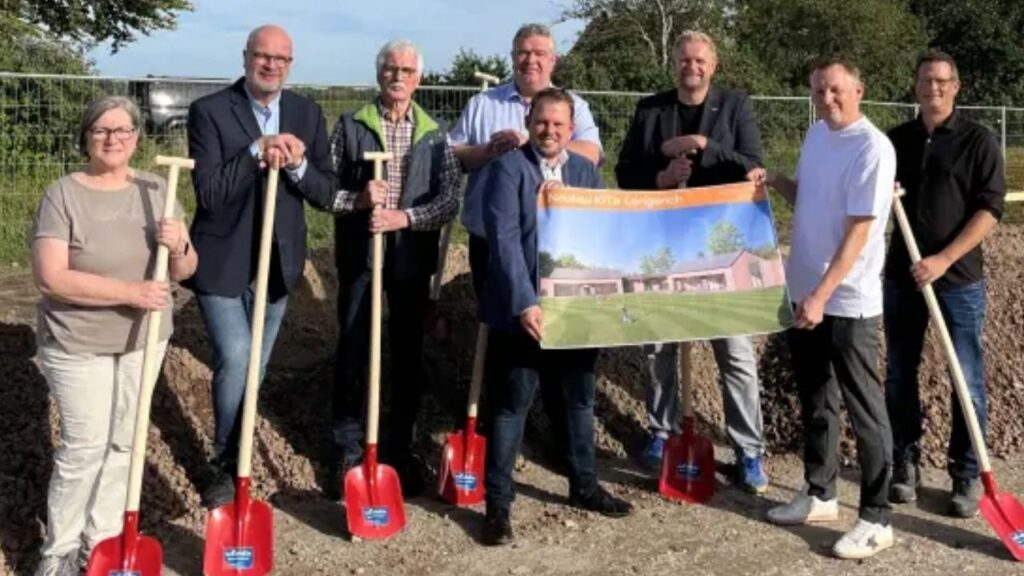 Personengruppe beim Spatenstich für Bauprojekt einer Kita mit großen Plakaten und roten Schaufeln.