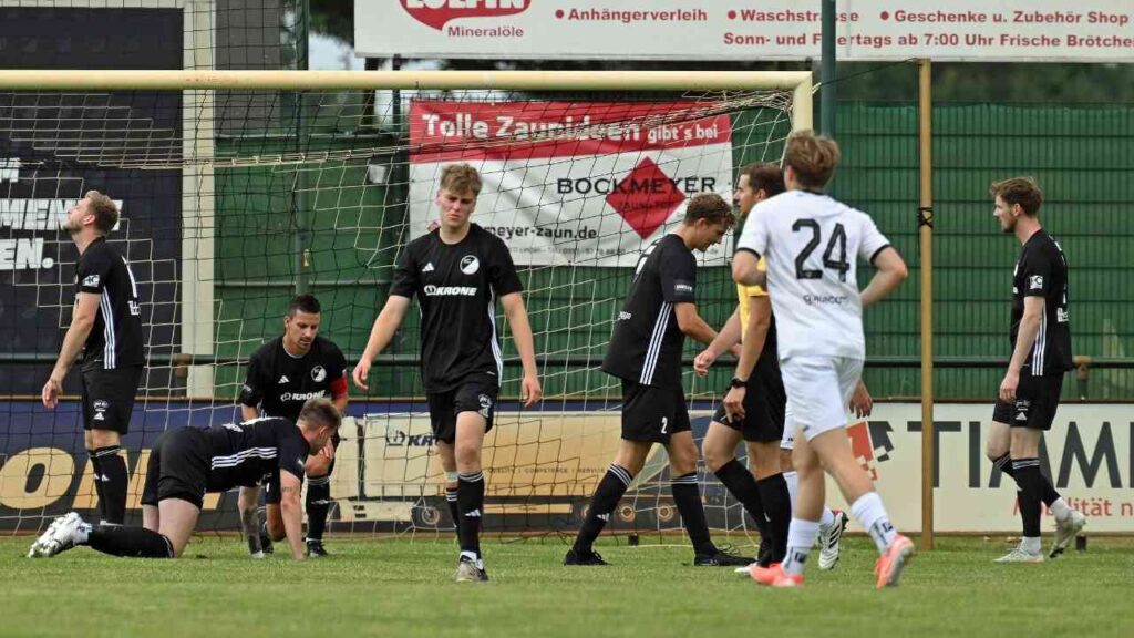 Fußballmannschaft in schwarzen Trikots nach Spielaktion vor dem Tor. Entscheidungen des Schiedsrichters werden diskutiert.