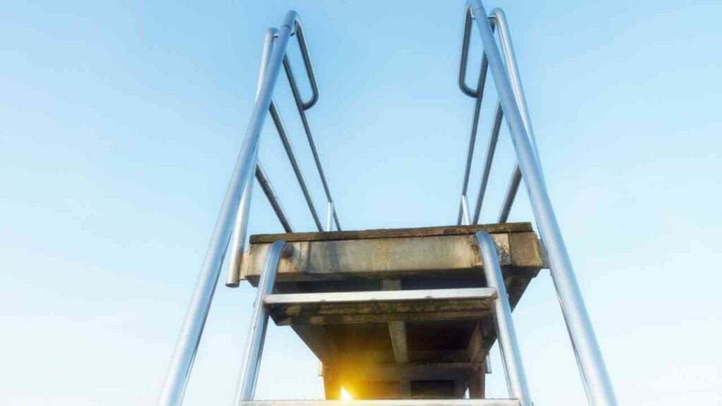 Sprungturm mit Metallleiter vor klarem Himmel und Sonnenlicht im Hintergrund. Ideal für Sommer- und Freizeitaktivitäten.