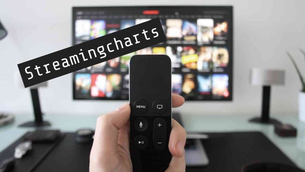 Fernbedienung vor unscharfem TV-Bildschirm mit Streaming-Inhalten, Schriftzug Streamingcharts im Vordergrund.