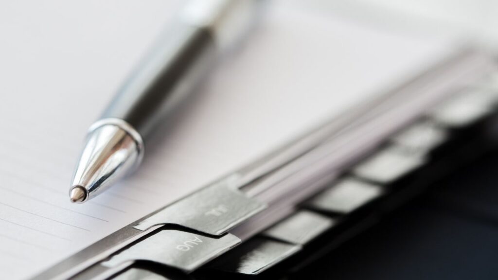 Kugelschreiber auf Notizbuch neben Laptop-Tastatur, Symbol für Tagesordnung.