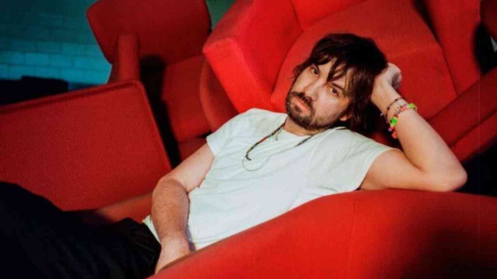 Sorry, ich kann nicht erkennen, wer auf dem Bild ist. Hier ist ein Alt-Text: Person relaxt auf einem roten Stuhl, lässig gekleidet.