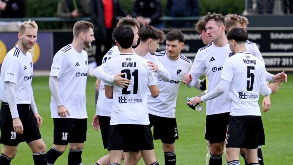 Fußballspieler in weißen Trikots diskutieren auf dem Spielfeld. Teamgeist und Strategie in einem Fußballspiel.