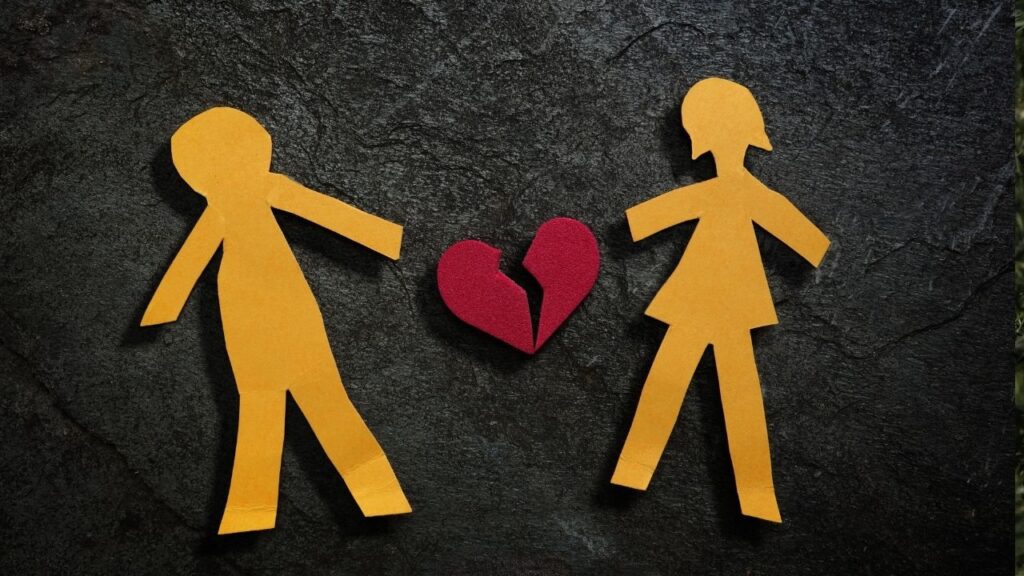 Papierfiguren mit gebrochenem Herz, symbolisieren Trennung auf dunklem Hintergrund.