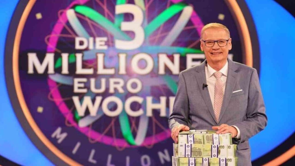 Moderator mit Geldbündeln auf der Bühne der Show Die 3 Millionen Euro Woche, bunte Hintergrundbeleuchtung.