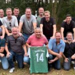 Männergruppe im Freien mit Trikot von Olympia Uelsen, Nummer 14, grünem Hintergrund, Herbststimmung, lächelnd.
