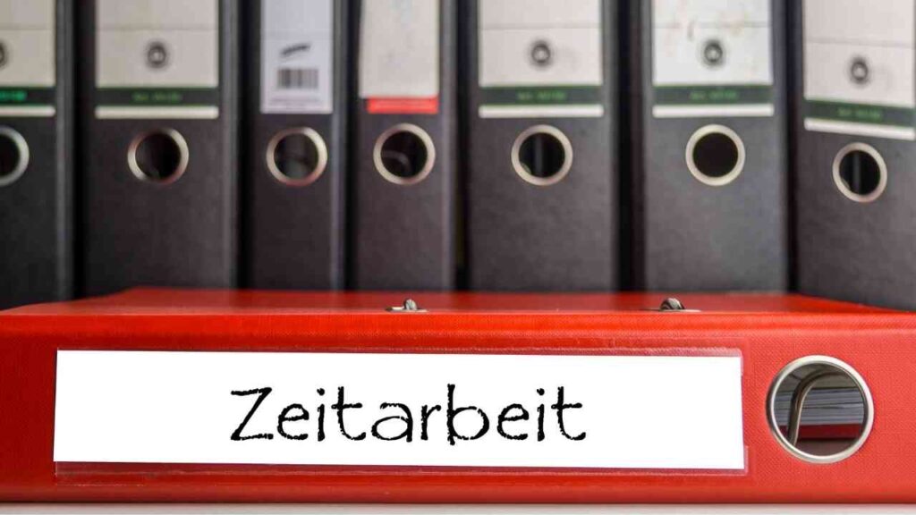 Roter Aktenordner mit der Aufschrift Zeitarbeit vor einer Reihe von schwarzen Ordnern im Hintergrund.