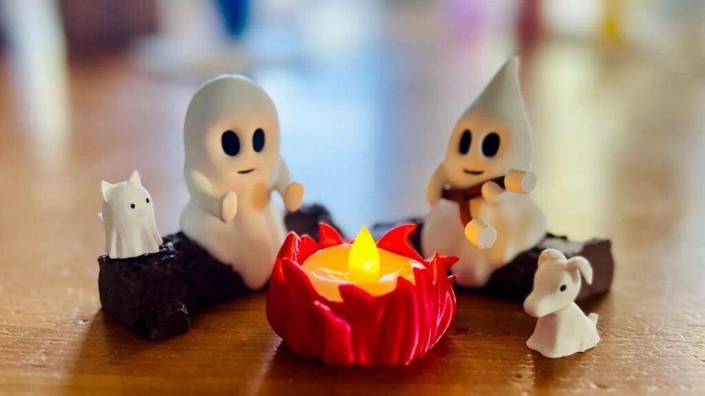 Süße Geisterfiguren sitzen um LED-Kerze in roter Halterung auf Holztisch, herbstliche Deko-Atmosphäre.