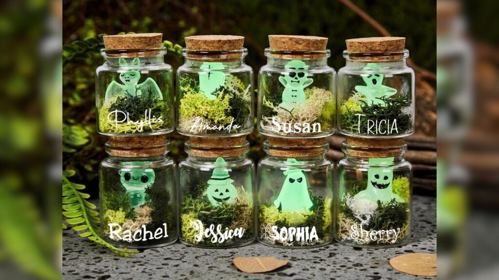 Glasflaschen mit leuchtenden Halloween-Miniaturen: Geister, Kürbisse und Namen auf Moos. Stimmungsvolle Deko.