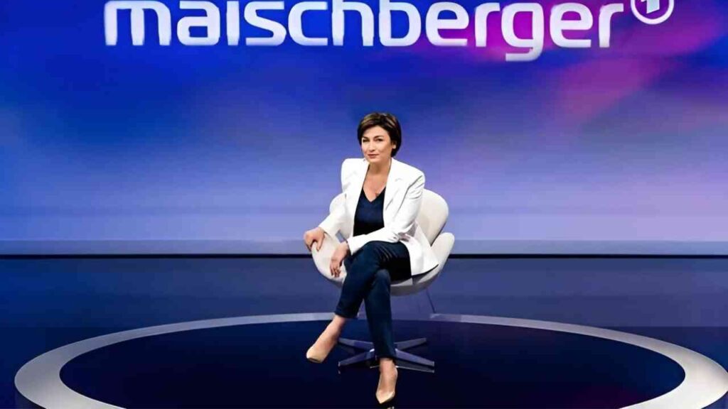Person in weißem Blazer sitzt auf einer Bühne bei Maischberger-Talkshow, blauer Hintergrund mit Logo.