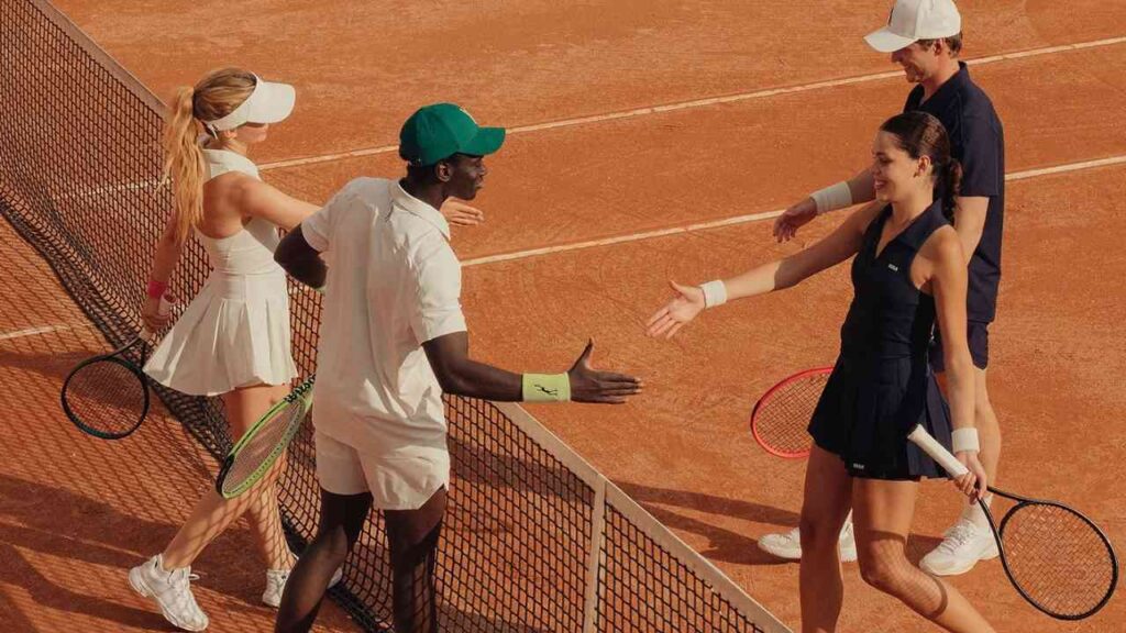 Tennisspielerinnen und Tennisspieler geben sich nach einem Match auf Sandplatz die Hand am Netz.