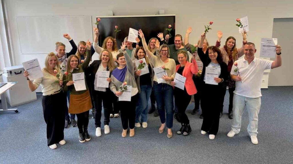 Gruppe von Menschen mit Urkunden und Blumen feiern in einem Büro. Glückliche Gesichter, Erfolg und Teamgeist.