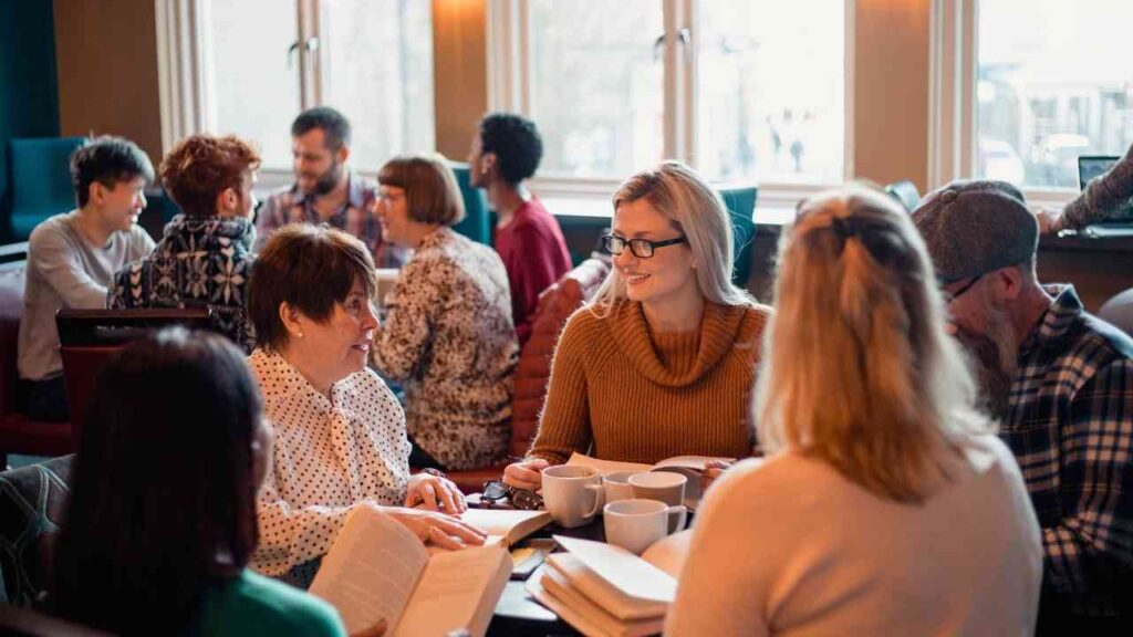 Menschen in einem Café diskutieren in Gruppen, Bücher und Kaffee auf dem Tisch, entspannte Gesprächsatmosphäre.