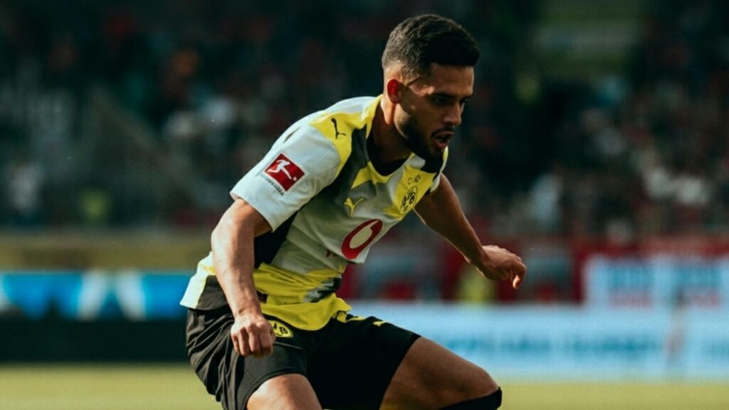 Fußballspieler in gelb-schwarzem Trikot dribbelt dynamisch über das Spielfeld bei einem Spiel.