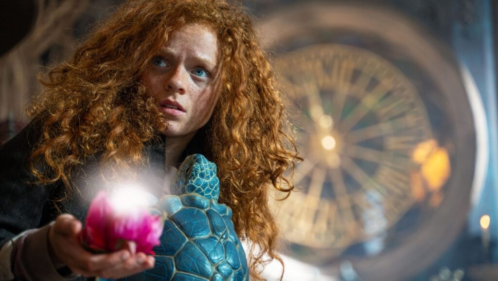 Ein Mädchen mit lockigem rotem Haar hält eine leuchtende Blume und eine blaue Schildkröte in einer fantastischen Umgebung.