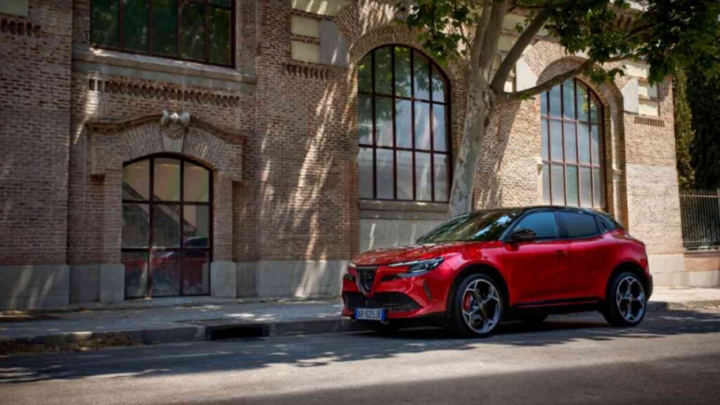 Roter Alfa Romeo Junior SUV parkt vor einer Backsteinmauer mit großen Fenstern.