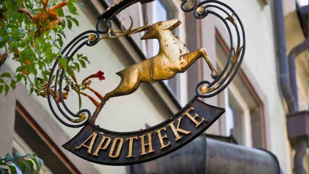 Ein goldener Apothekerschild mit einem springenden Reh und dem Wort 'Apotheke' in schwarzer Schrift.