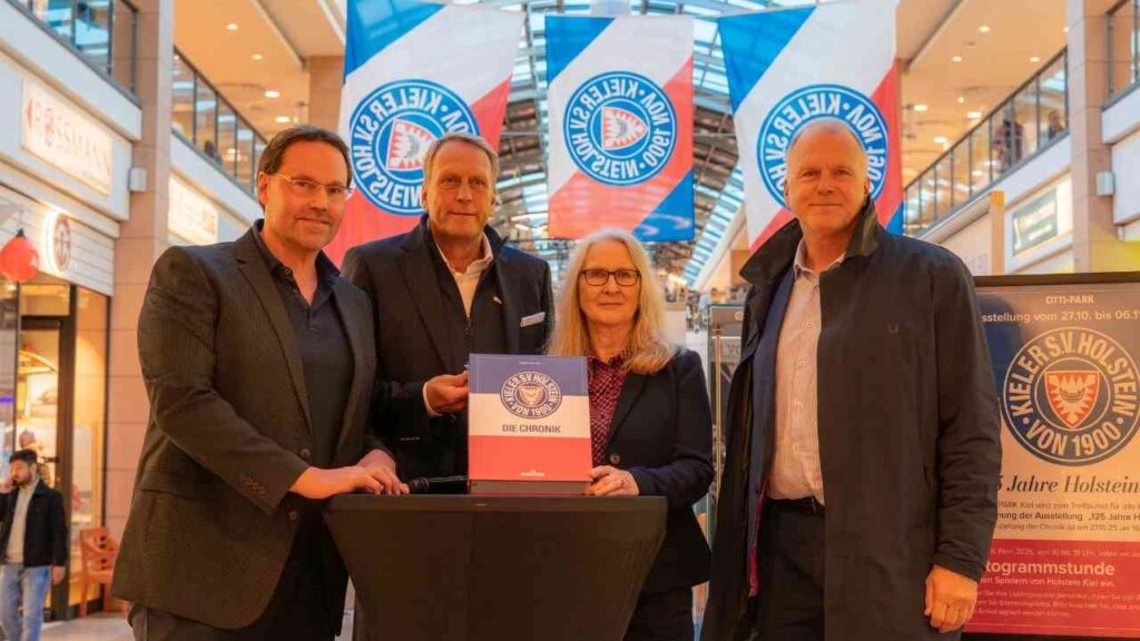 Vier Personen präsentieren ein Buch über die Geschichte von Kieler Holstein im Einkaufszentrum.