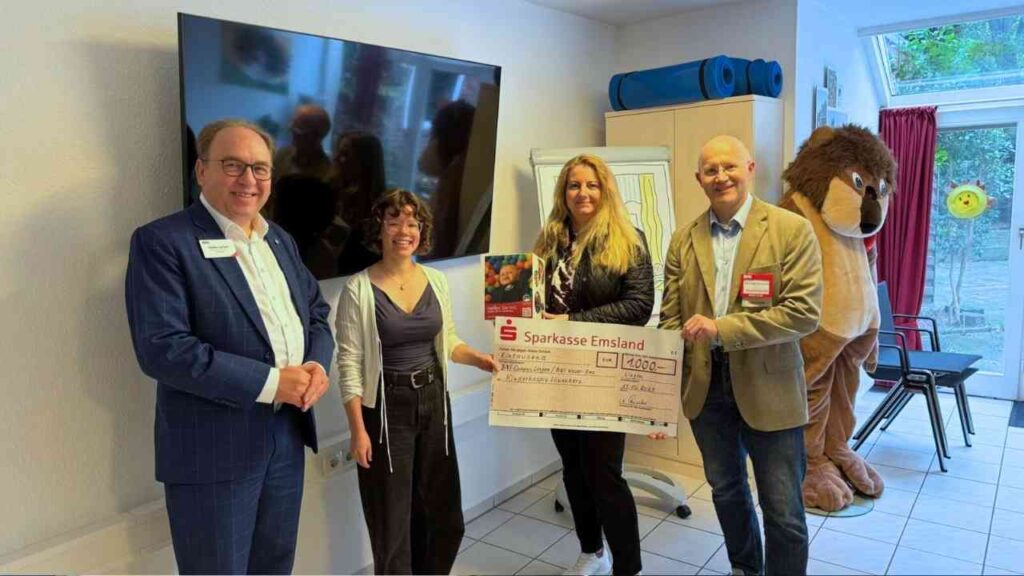 Gruppenfoto mit vier Personen, die einen großen Scheck der Sparkasse Emsland überreichen.
