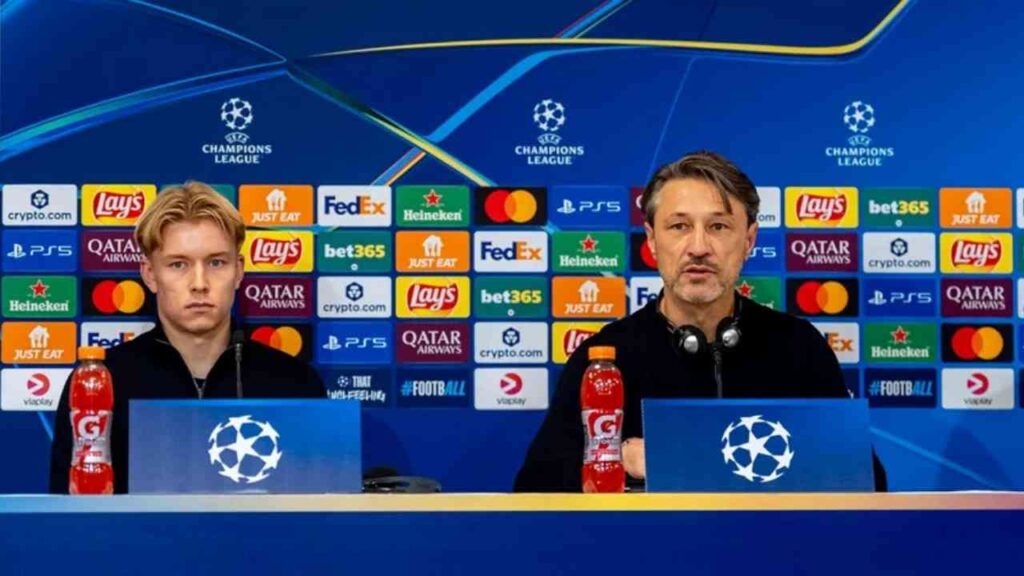 Pressekonferenz mit zwei Männern, einem Spieler und einem Trainer, im Champions-League-Setting mit Sponsorenlogos im Hintergrund.