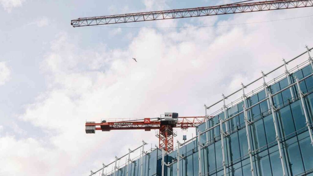 Baukran über einem modernen Gebäude mit Glasfassade und blauem Himmel im Hintergrund.