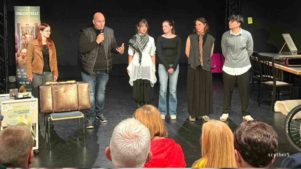 Eine Gruppe von fünf Personen steht auf einer Bühne während einer Benefizauktion in Lingen, mit einem Koffer im Vordergrund.