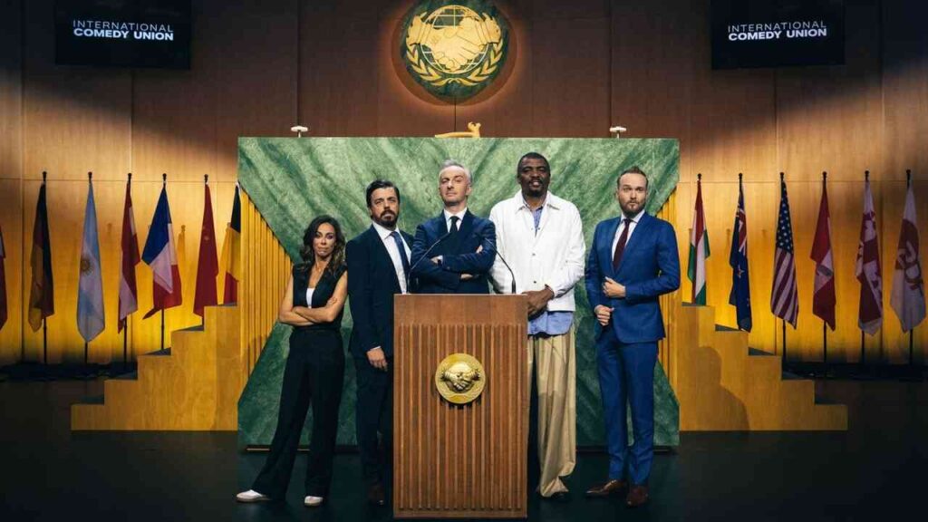 Fünf Personen stehen an einem Rednerpult vor einer Kulisse mit Flaggen und einem großen Emblem der Internationalen Comedy Union.