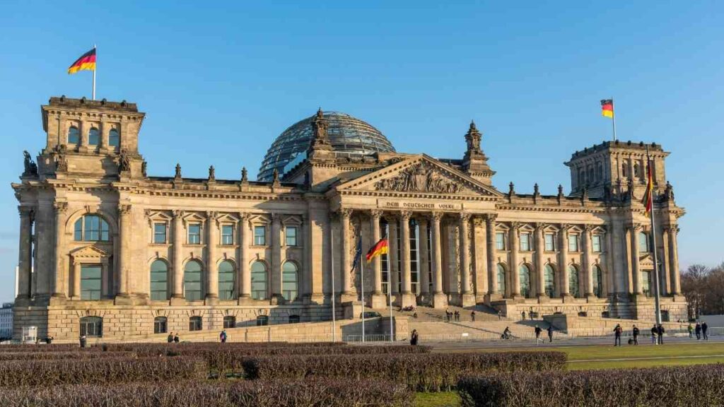Reichstagsgebäude in Berlin mit deutscher Flagge und Kuppel unter klarem Himmel.