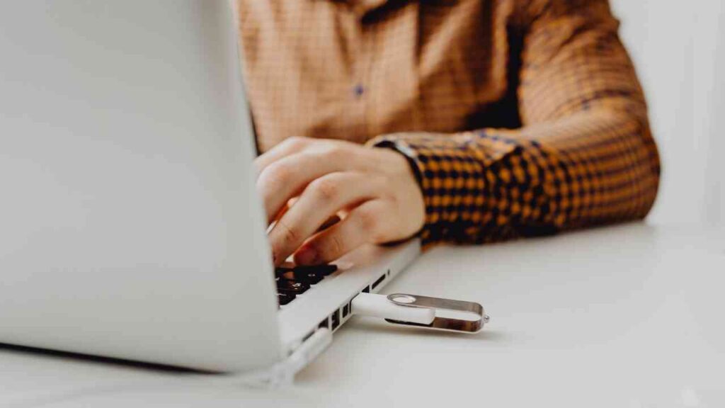 Person mit kariertem Hemd, die an einem Laptop arbeitet, während ein USB-Stick eingesteckt ist.