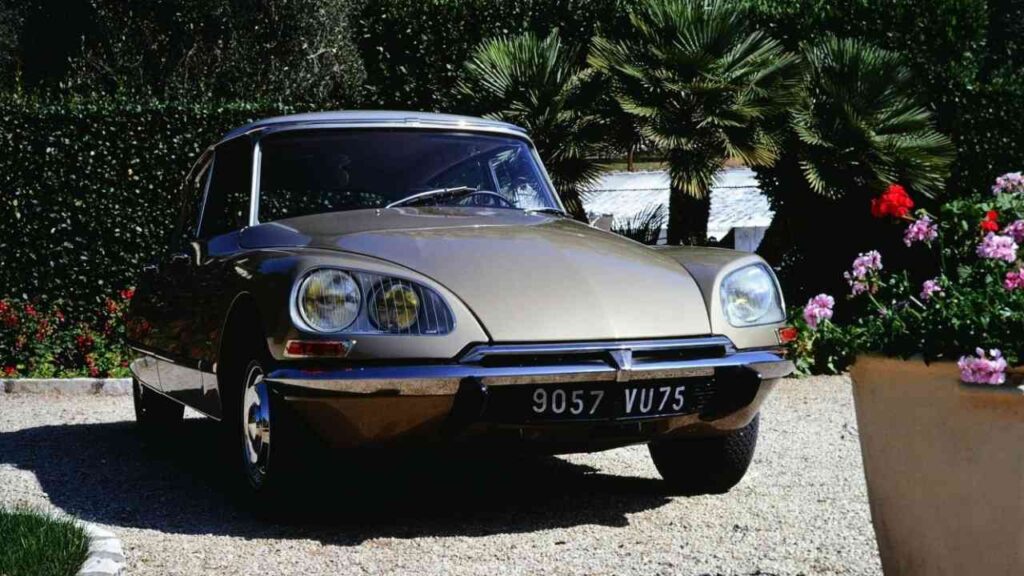Goldfarbener Citroën DS mit klassischem Design, geparkt in einer Gartenumgebung.