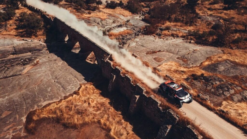 Rallyeauto fährt über eine steinerne Brücke in staubiger Landschaft, erzeugt Staubwolke. Abenteuer, Geschwindigkeit, Natur.
