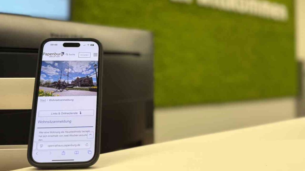 Smartphone zeigt die Webseite zur Wohnsitzummeldung in Papenburg mit einem Bild des Stadtplatzes.