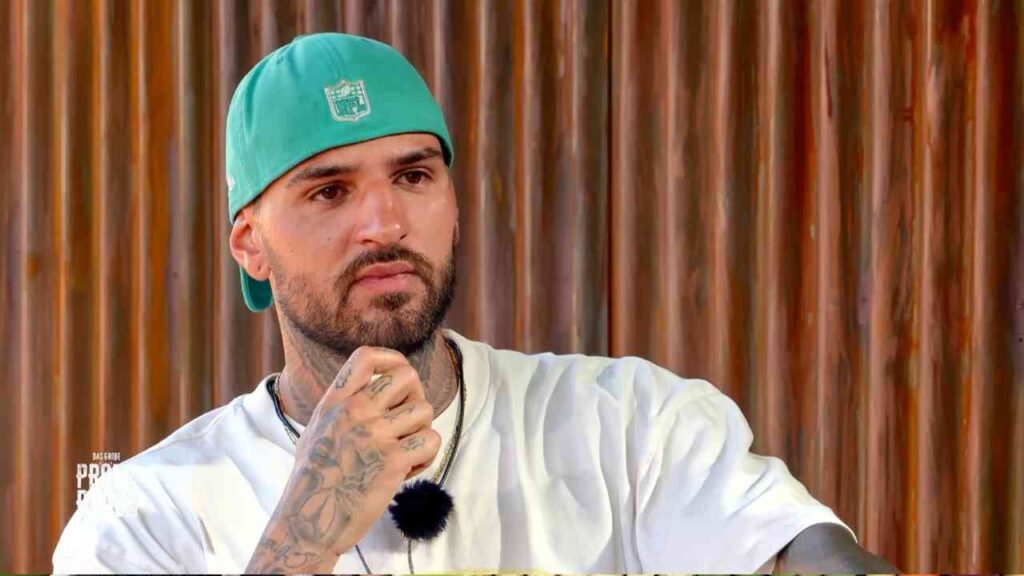 Mann mit tätowiertem Arm und grüner Kappe, der nachdenklich in die Kamera schaut.