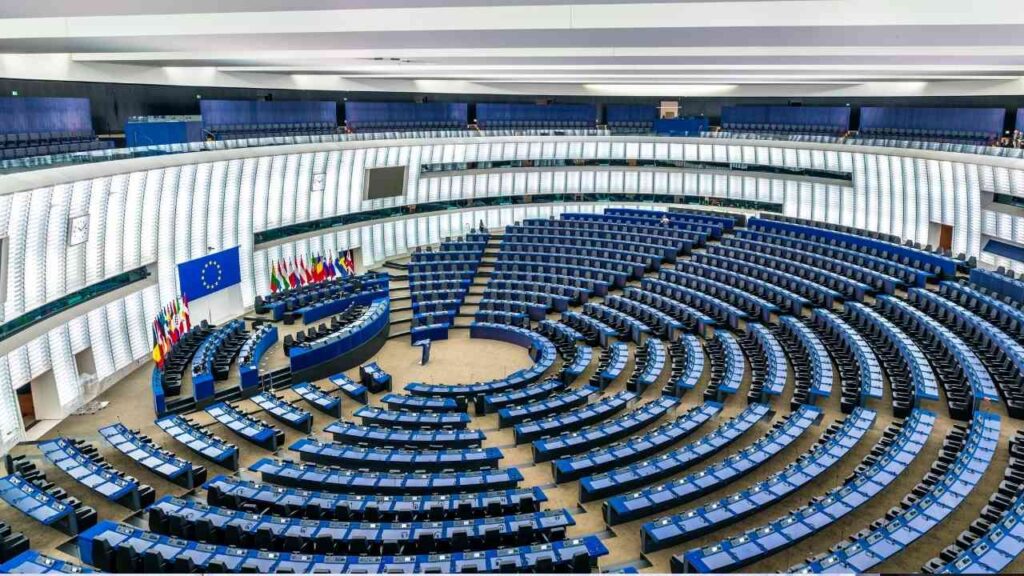 Plenarsaal des Europäischen Parlaments mit blauen Sitzen und Flaggen der Mitgliedstaaten.