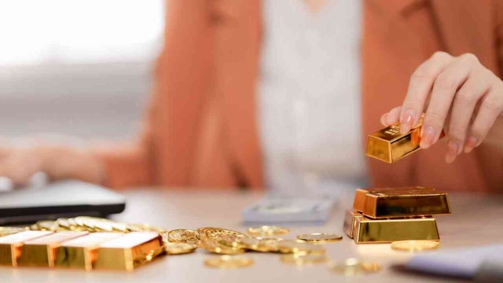 Eine Person, die Goldbarren und Goldmünzen auf einem Tisch anordnet, mit einem Laptop im Hintergrund.