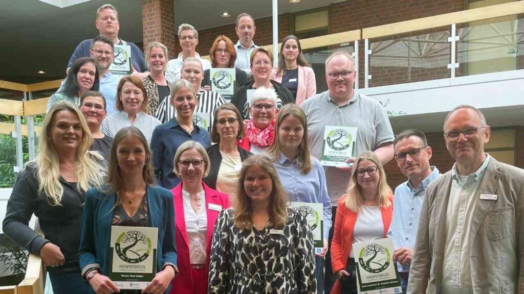 Mitarbeiter eines Unternehmens posieren mit Zertifikaten auf einer Treppe in einem modernen Gebäude.