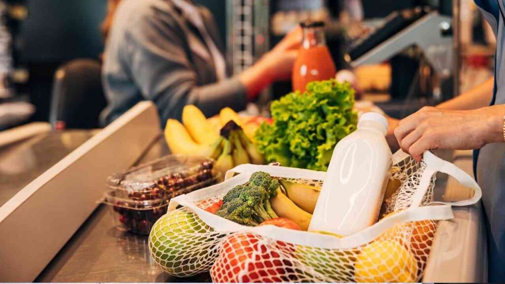 Einkaufswagen mit frischem Gemüse, Obst und einer Flasche Milch an der Kasse im Supermarkt.