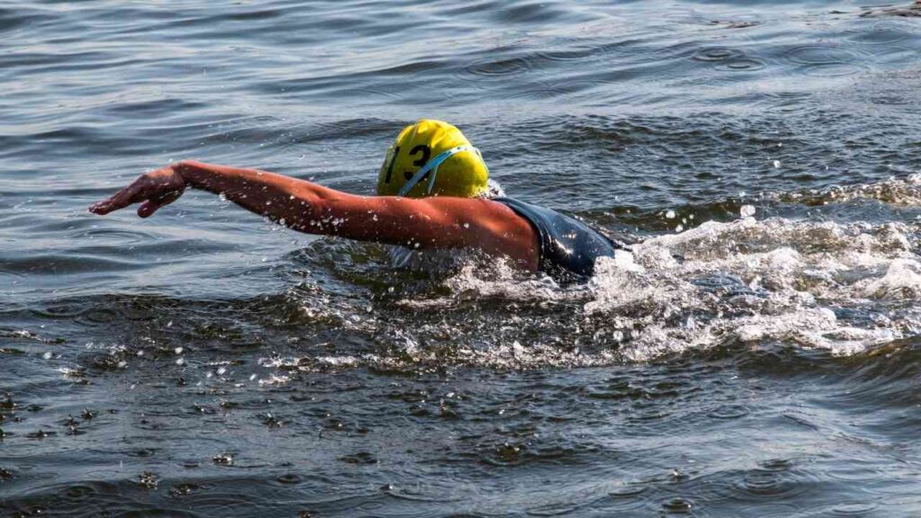 Ein Schwimmer mit gelber Badekappe schwimmt im Freiwasser und erzeugt Wellen.
