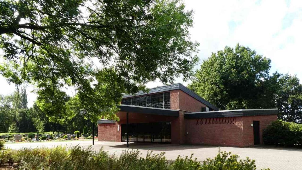 Moderne Friedhofskapelle aus roten Ziegeln mit großen Fenstern und einem überdachten Eingangsbereich.