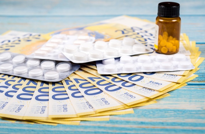 Zwei Blisterpackungen mit weißen Tabletten und ein Fläschchen mit gelben Tabletten auf einem Stapel von 200-Euro-Scheinen.
