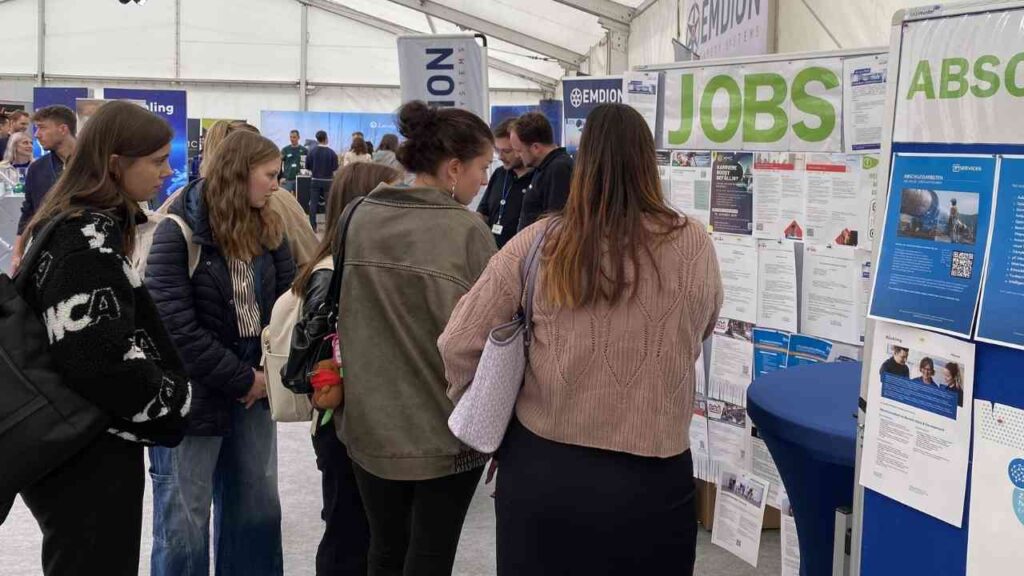 Gruppe von Personen, die an einem Job-Informationsstand in einer Zeltveranstaltung interessiert sind.