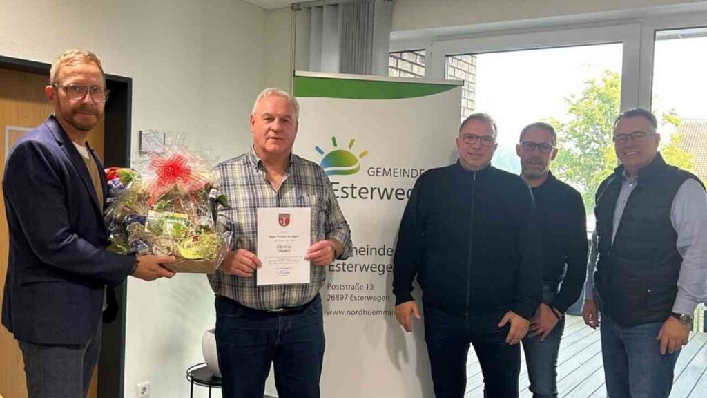 Eine Gruppe von vier Personen, die anlässlich eines Dienstjubiläums zusammenstehen, während einer Person eine Urkunde überreicht wird.