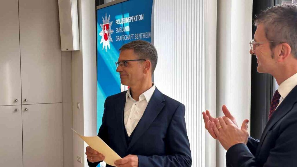Zwei Männer in formeller Kleidung, einer hält ein Dokument, während der andere applaudiert.