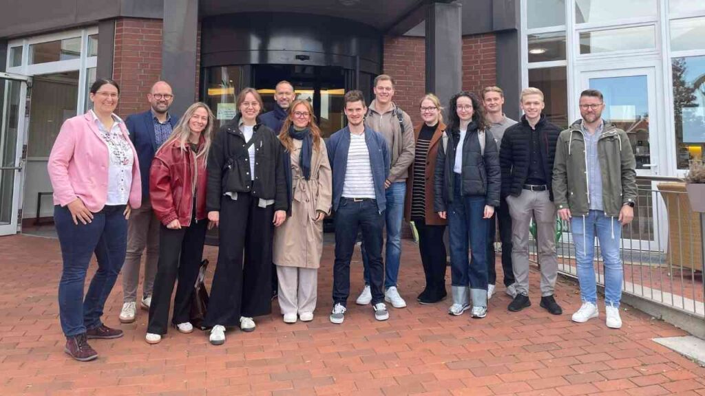 Gruppe von Personen, die vor dem St. Vinzenz Hospital stehen, in formeller und legerer Kleidung.