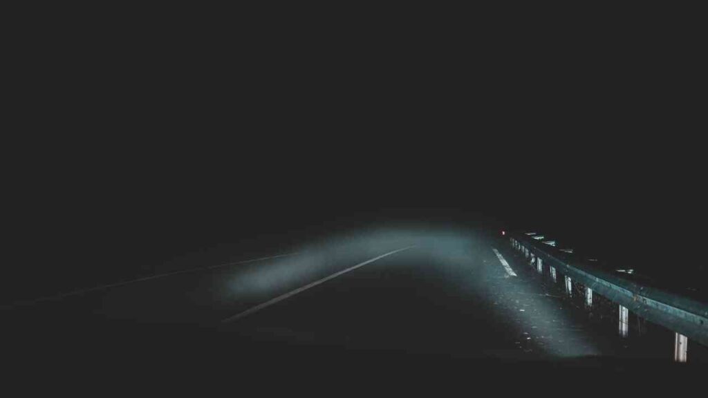Eine Landstraße in der Nacht, umgeben von dichtem Nebel und schwachem Licht.