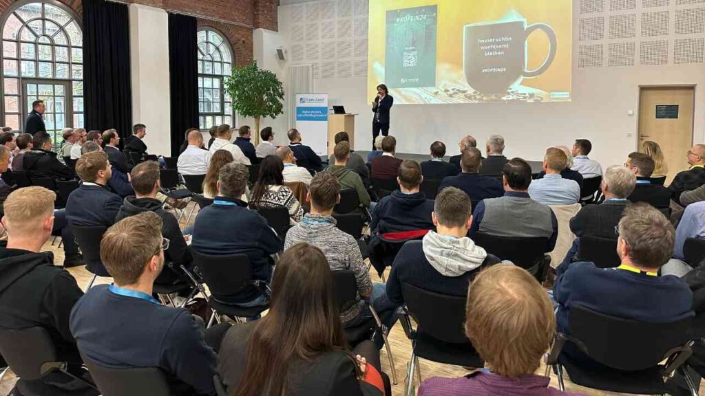 Eine Präsentation während einer Konferenz mit einem Redner und einem Publikum von Fachleuten im Hintergrund.