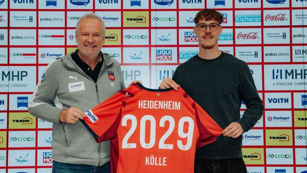 Adam Kölle hält ein Trikot mit der Aufschrift 'Heidenheim 2029' in der Hand, während er neben einem Vereinsvertreter steht.