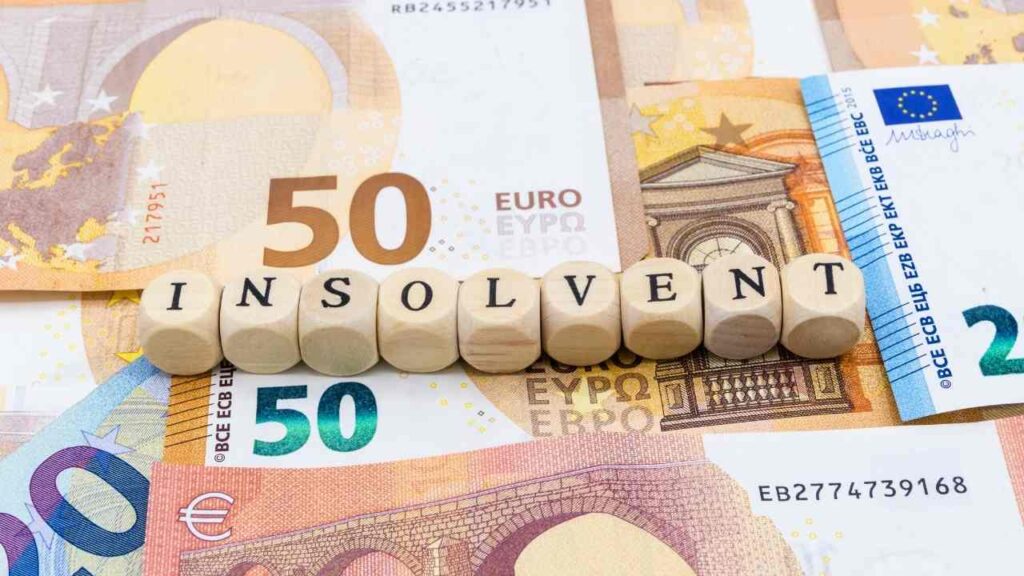 Holzbuchstaben bilden das Wort 'INSOLVENT' auf einem Hintergrund aus 50-Euro-Scheinen.